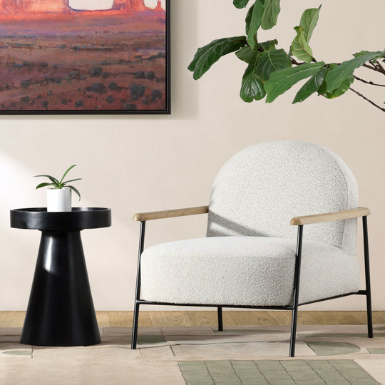 Modern living room with white armchair, black side table, and framed artwork of a desert landscape.