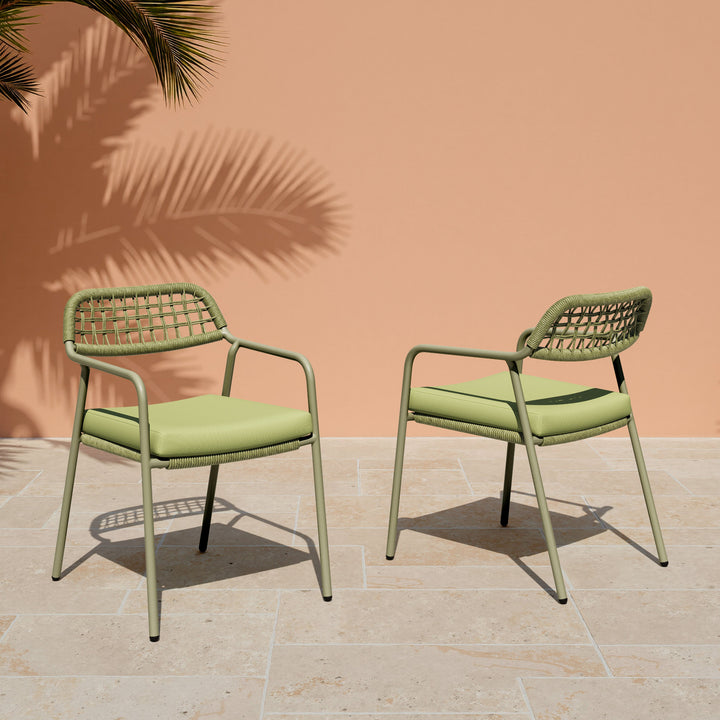 Two green chairs with cushioned seats on a tiled patio with a peach wall and palm leaf in the background.