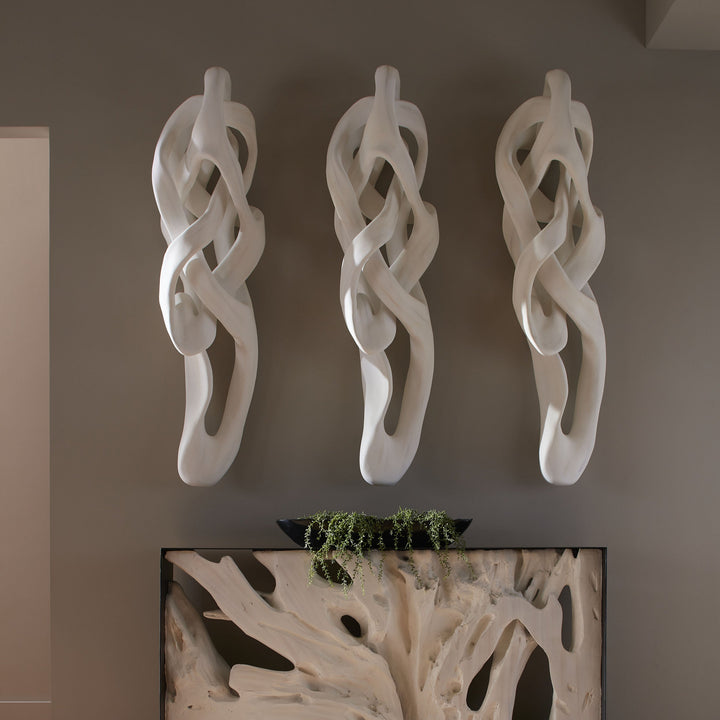 Three white abstract wall sculptures on a gray wall with a decorative plant box below.