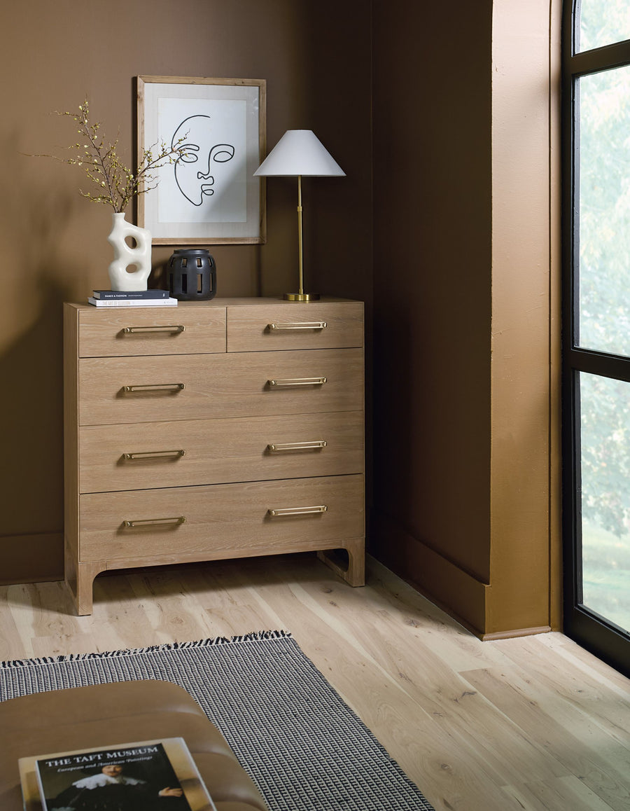 Wooden five-drawer dresser with a natural finish, set in a stylish bedroom.