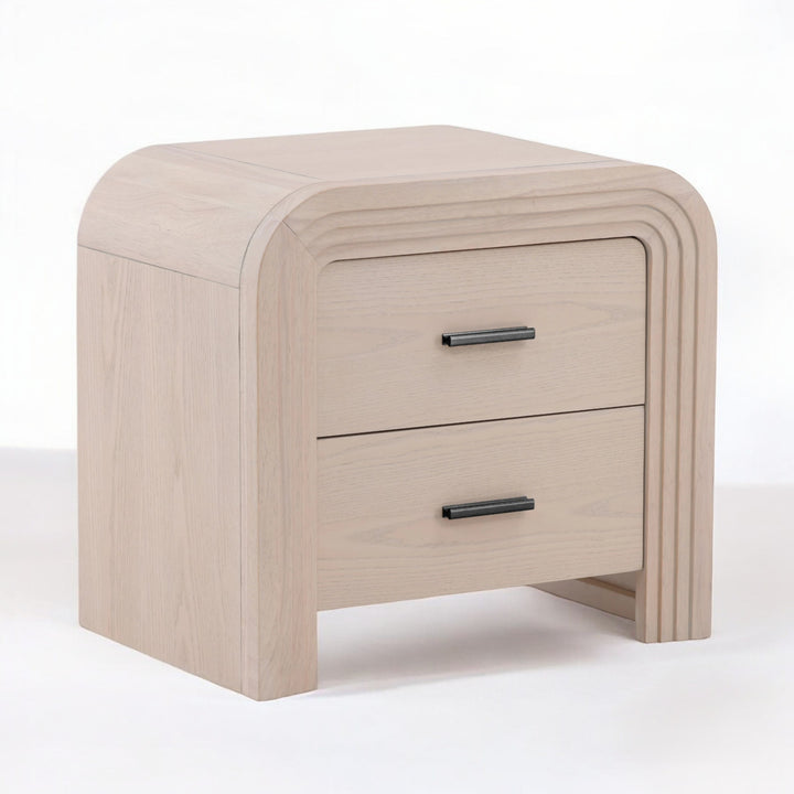 Angled view of a modern light wood nightstand with a curved design featuring two drawers and sleek black handles.