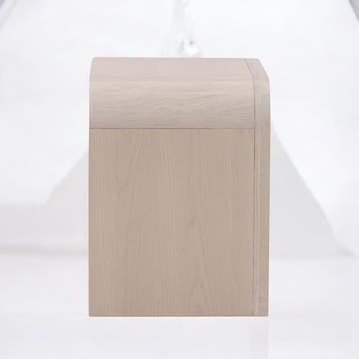 Side view of a modern light wood nightstand with a curved design featuring two drawers and sleek black handles.