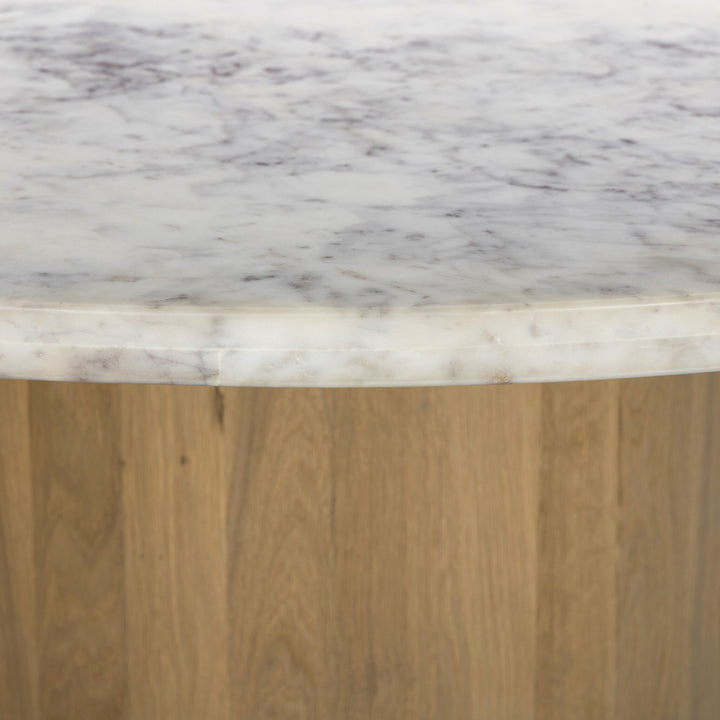 Close-up of a round white marble table top with subtle gray veining, resting on a warm wooden base.