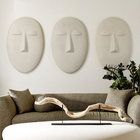 Modern living room with a white oval coffee table, gray sofa, and decorative wall masks.