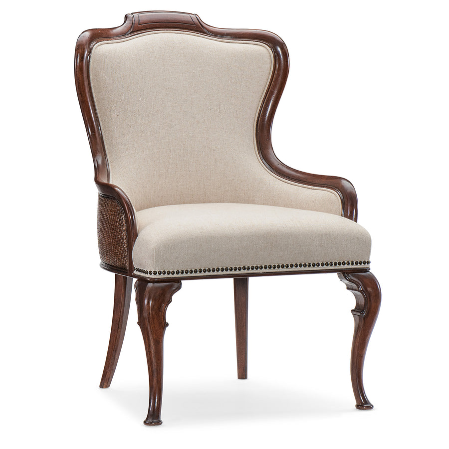 A classic wingback armchair with a dark brown carved wood frame, beige textured fabric upholstery, and decorative nailhead trim
