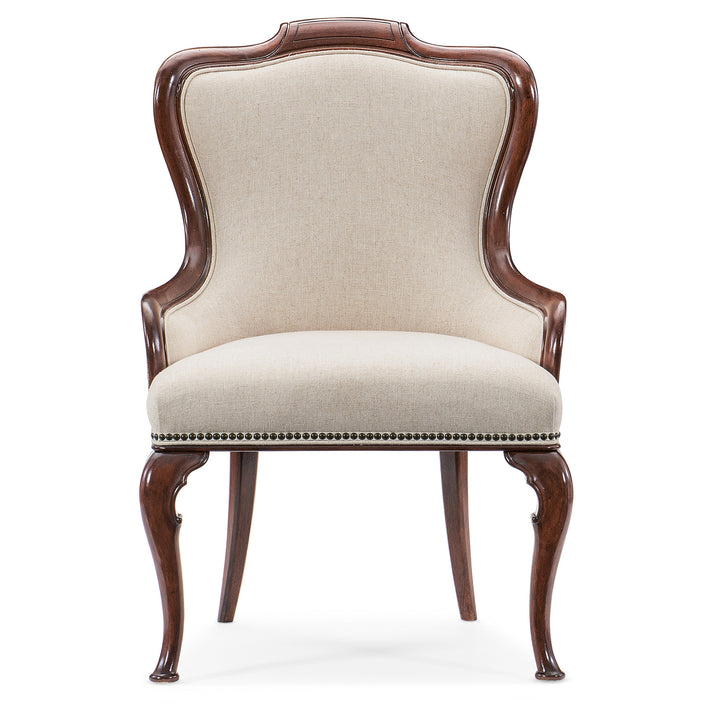 An upholstered arm chair with beige fabric, bronze nailhead trim, and carved cabriole legs finished in cherry wood.