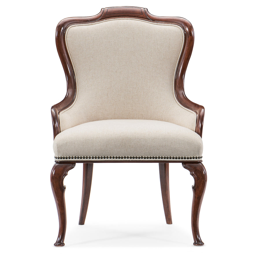 An upholstered arm chair with beige fabric, bronze nailhead trim, and carved cabriole legs finished in cherry wood.