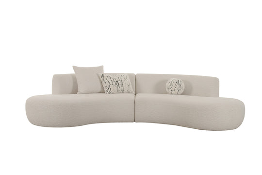 Modern curved beige sofa with textured fabric, featuring two patterned cushions and a round decorative pillow.