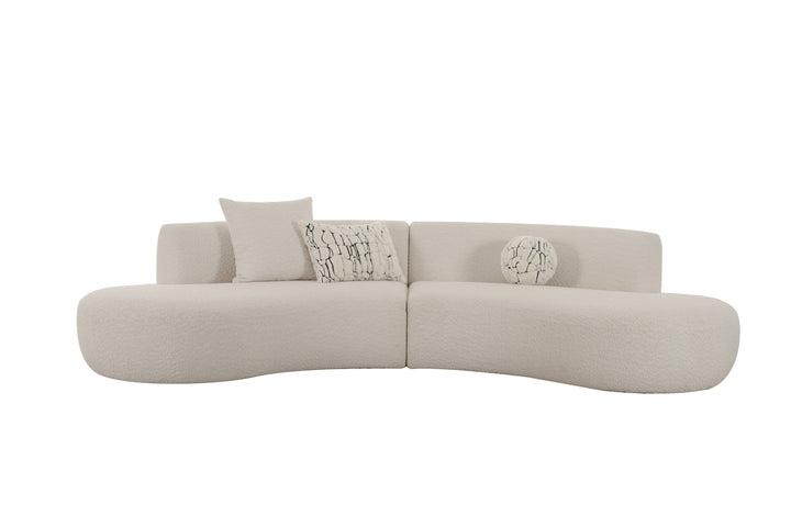 Modern curved beige sofa with textured fabric, featuring two patterned cushions and a round decorative pillow.