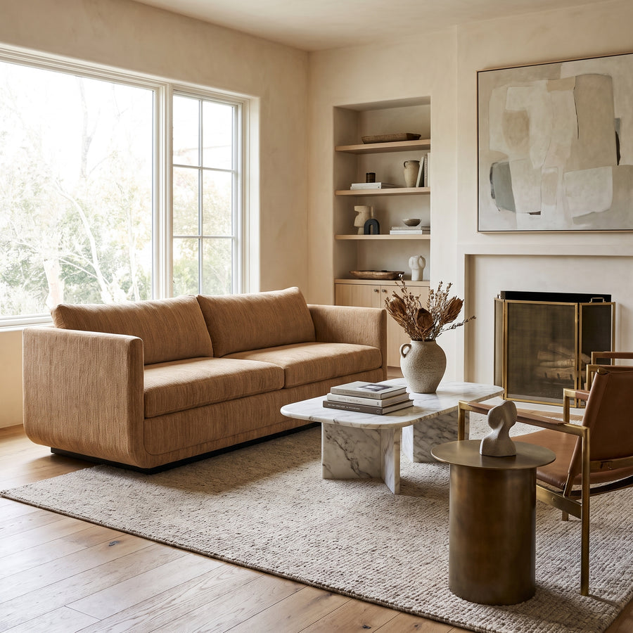 Modern minimalist living room featuring a tan sofa, marble coffee table, fireplace, and neutral decor in a warm, airy space.