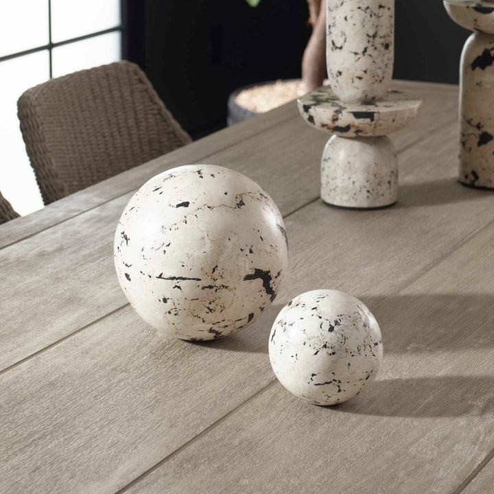Two marble-like spherical objects on a wooden surface with a blurred indoor background.