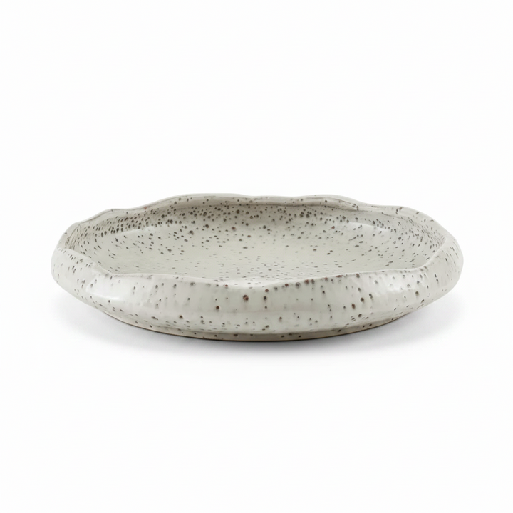 A shallow, round ceramic decorative bowl with a scalloped rim, featuring a speckled glaze in a light gray and off-white color combination.