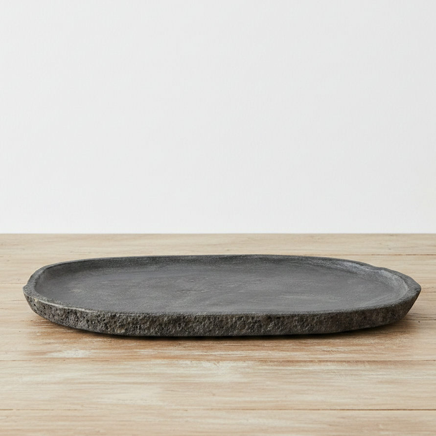 A decorative stone tray with a textured, rustic edge, placed on a light wood surface against a plain white background.