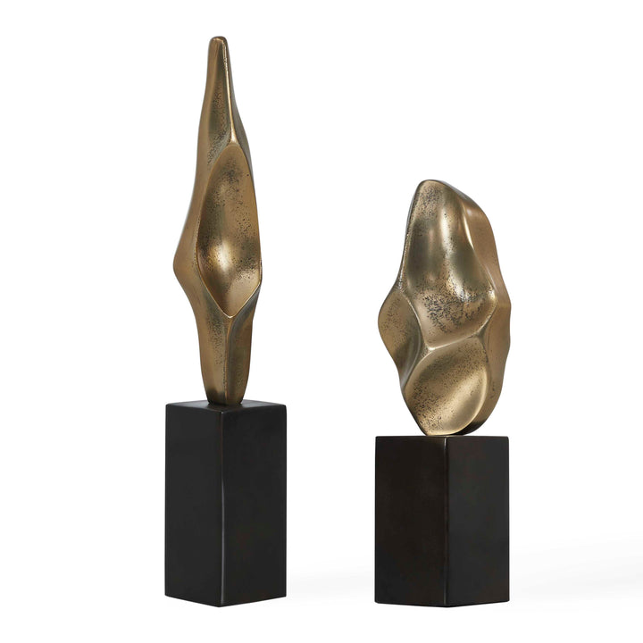 Two abstract metallic gold decorative sculptures on black rectangular pedestals