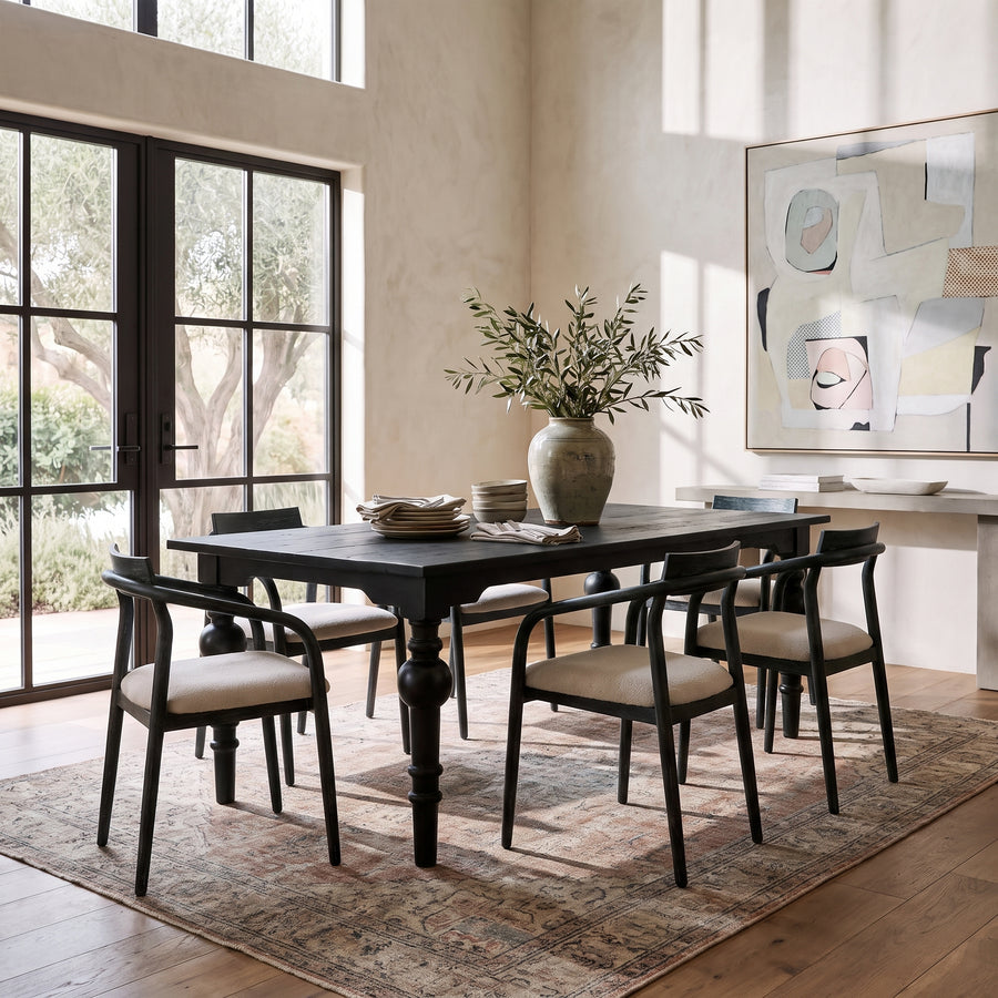 Modern rustic dining room with a black wood table, upholstered chairs, olive branch centerpiece, and abstract wall art.