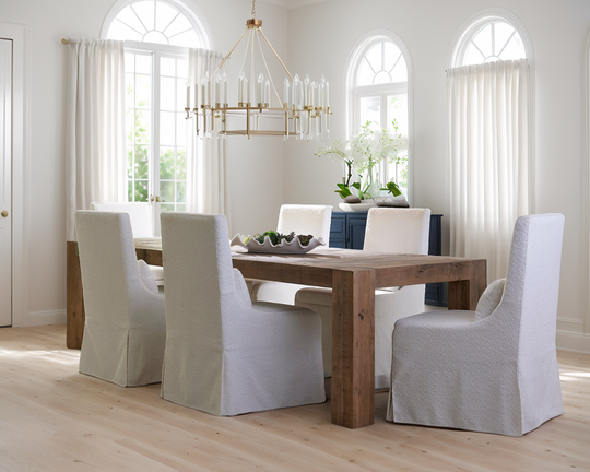 Dining room with wooden table and white chairs in a bright room with large windows.