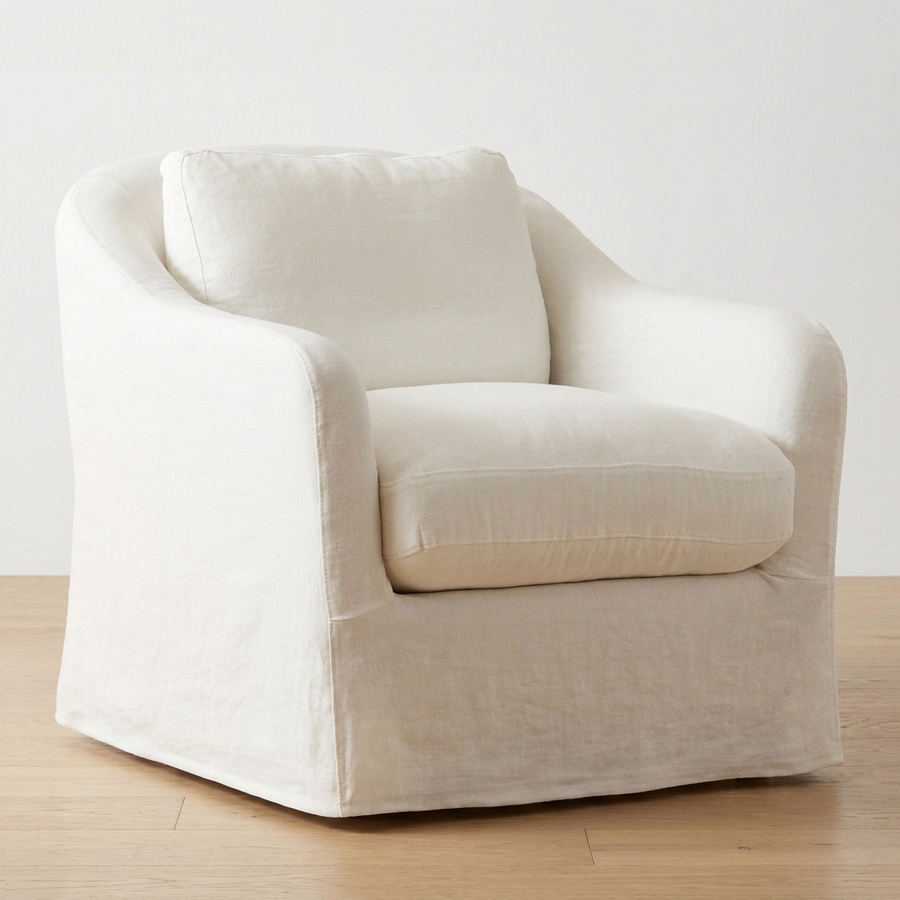 An off-white slipcovered armchair, set against a plain white wall on a light wood floor.