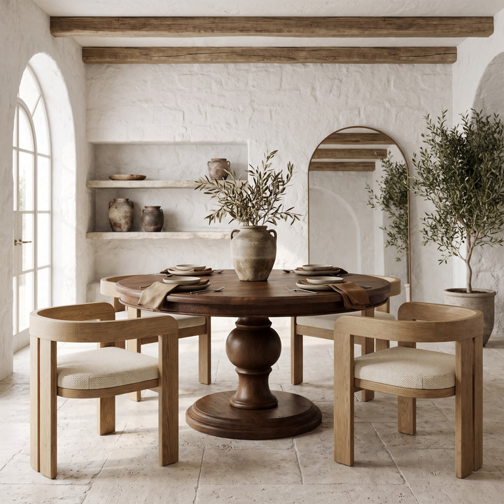 Mediterranean-style dining room with a round wooden table, modern oak chairs, stone walls, and arched architectural details.