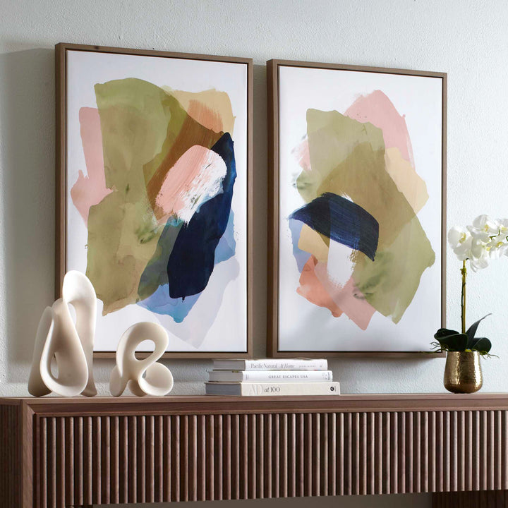 Two abstract art pieces on a wall above a wooden console table with decorative items.