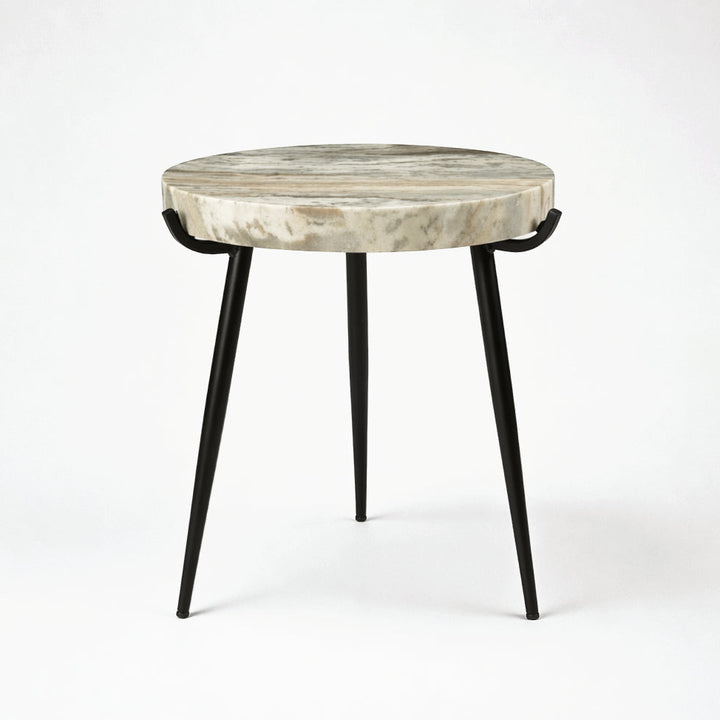 A round side table with a natural stone top featuring beige and gray marbling, supported by three slim black metal legs.