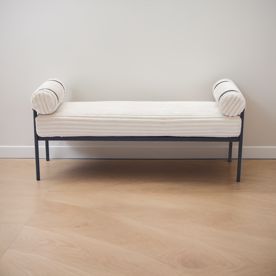White bench with black metal frame against a plain wall.