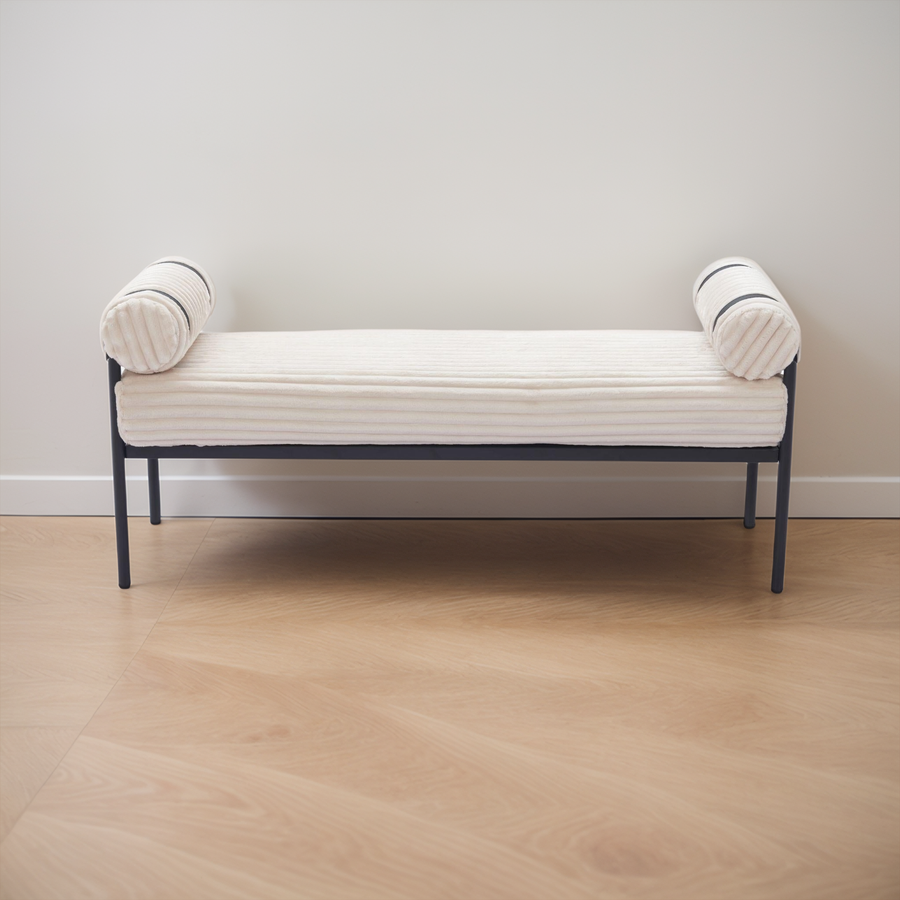 White bench with black metal frame against a plain wall.