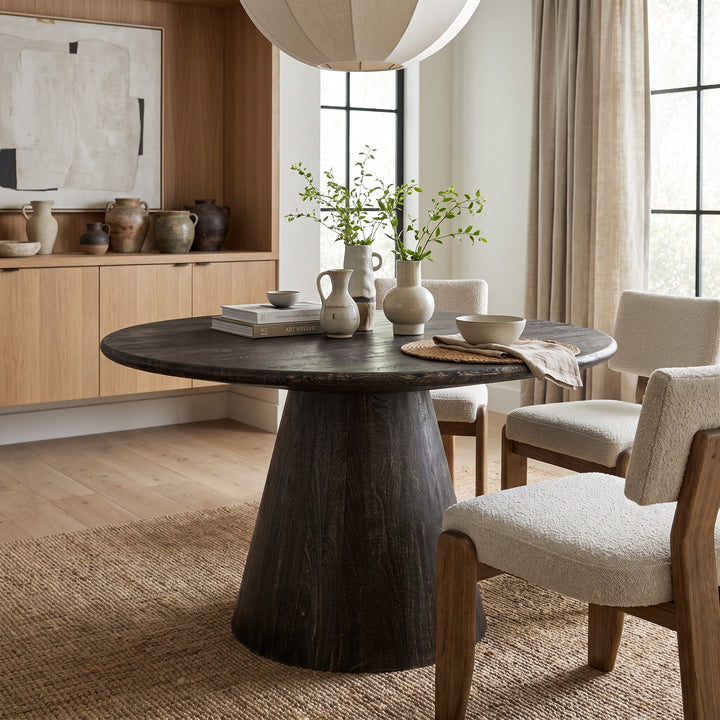 Modern dining room with a dark wood pedestal table, cream textured chairs, and minimalist organic decor in a bright space.
