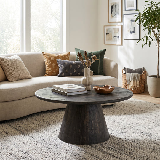 A round dark wood coffee table with a tapered pedestal base