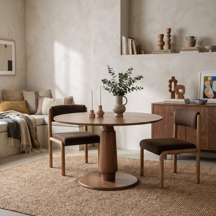 Modern minimalist dining room with a round wooden table, brown chairs, and neutral decor in a warm, cozy interior.