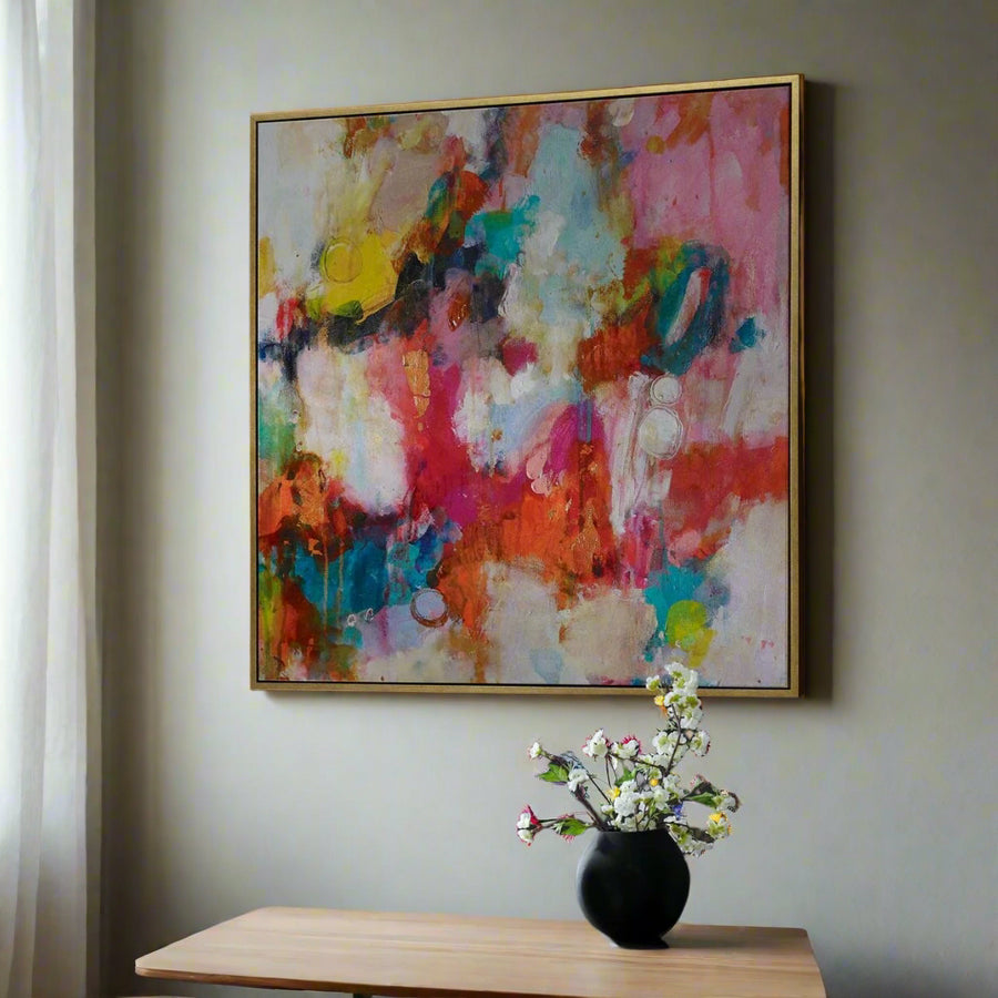Abstract colorful painting on a wall above a wooden table with a vase of flowers.