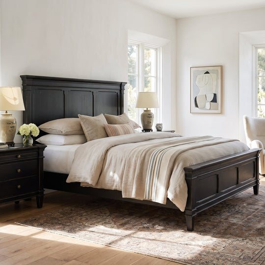 Modern farmhouse bedroom featuring a black wooden bed frame, neutral bedding, matching nightstands, and a cozy accent chair.