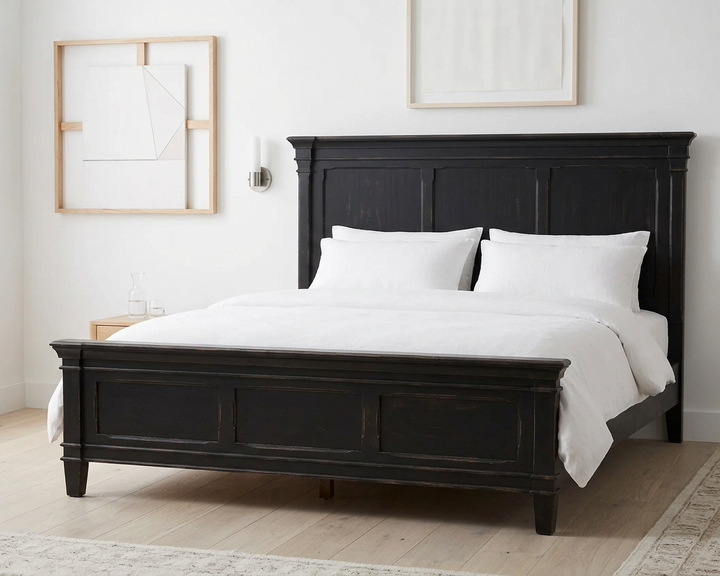 A black wooden bed frame with a tall panel headboard and footboard, styled with white bedding and pillows
