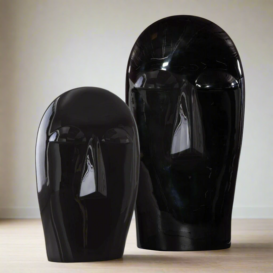 Two black ceramic face sculptures on a neutral background