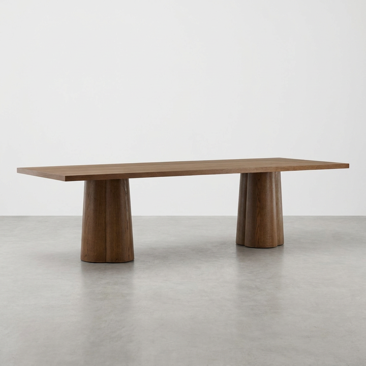 A modern rectangular wooden dining table with a medium brown wood grain finish, supported by two chunky, tapered cylindrical pedestal bases