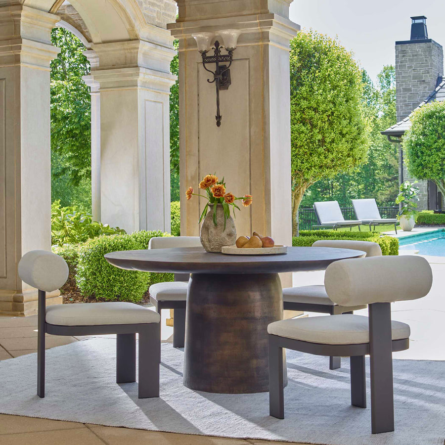 Outdoor dining set with a round table and chairs on a patio with greenery and a pool in the background.