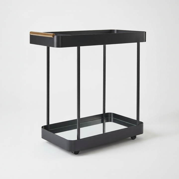 A modern two-tier bar cart in matte black metal with a clear glass lower tray and a gold top handle, shown on a plain light gray background.