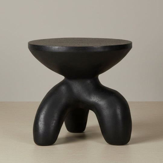 Black, modern-styled stool on a beige surface with a neutral background