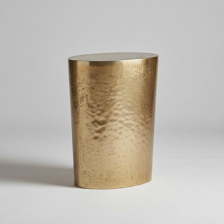 A tapered oval side table with a metallic gold finish, shown on a light gray studio background.