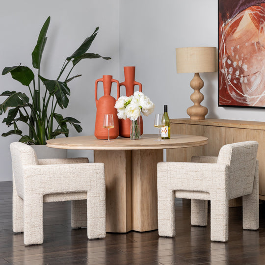 Modern dining room with round wooden table, chairs, and decorative items.