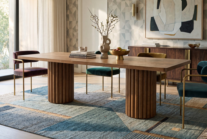 Modern dining room featuring a fluted wooden pedestal table, colorful velvet chairs, and a geometric area rug.
