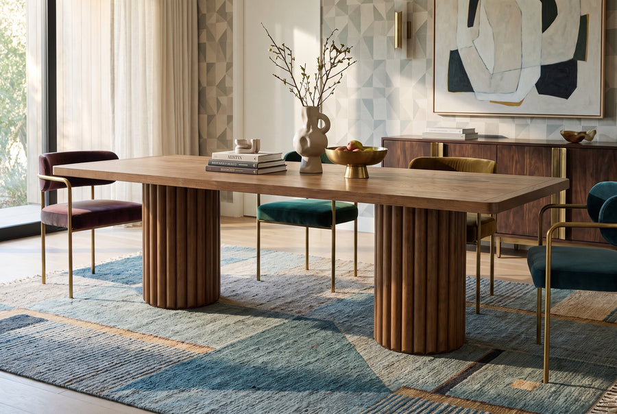 Modern dining room featuring a fluted wooden pedestal table, colorful velvet chairs, and a geometric area rug.