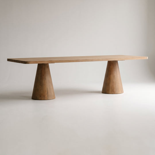 A minimalist wooden dining table with a rectangular top and two tapered cone-shaped legs, shown on a white studio background.