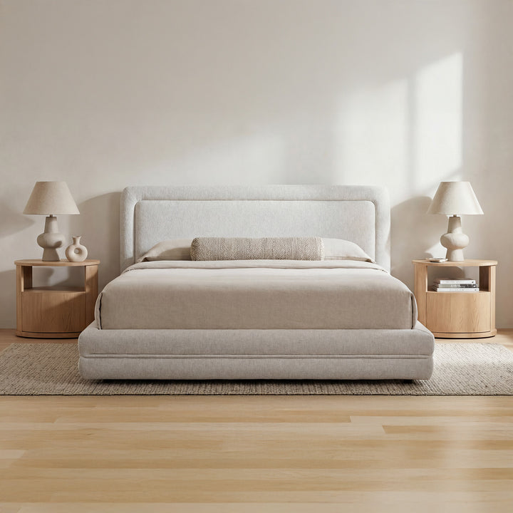 Beige upholstered bed in a minimalistic bedroom with wooden nightstands and lamps.