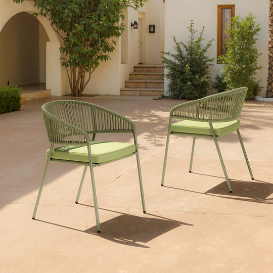 Two green outdoor chairs on a patio with a building and plants in the background