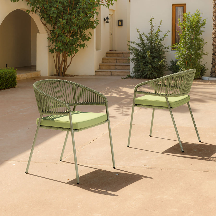 Two green outdoor chairs on a patio with a building and plants in the background