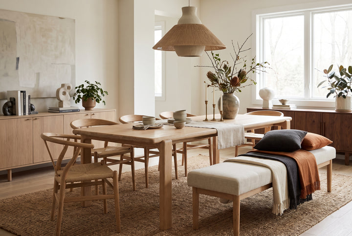 Modern minimalist dining room with light wood furniture, woven pendant light, and a cozy bench in a neutral, earthy palette.