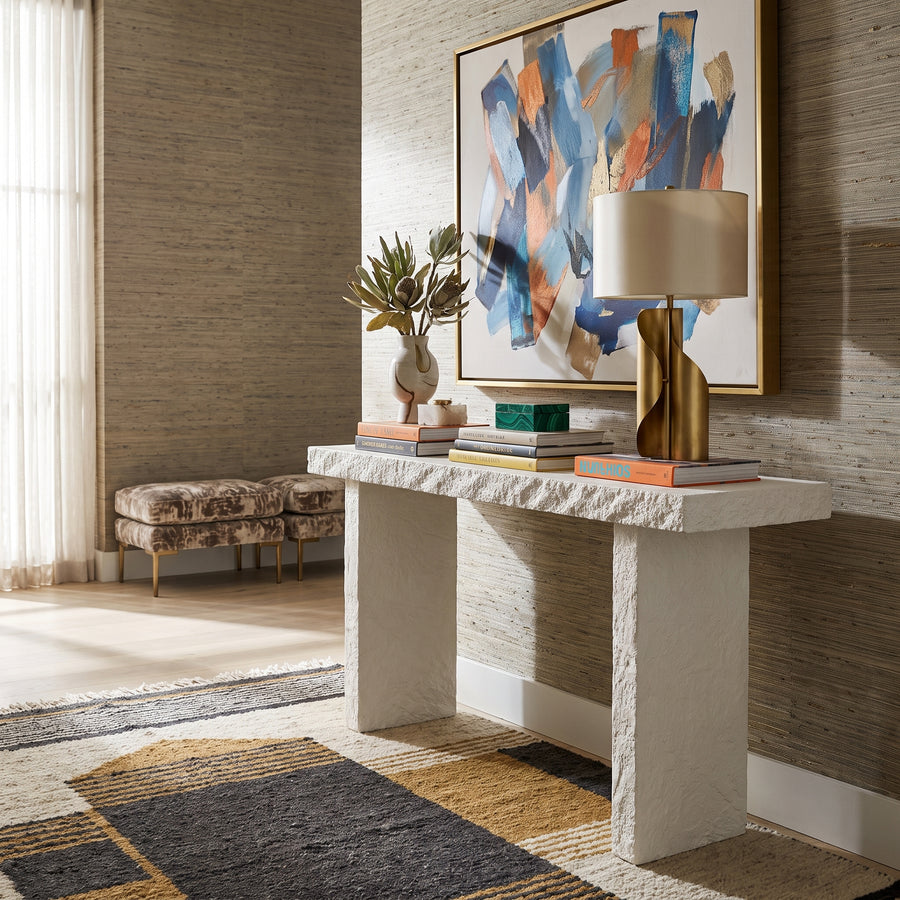 Hagan Limestone Console Table styled in a modern entryway with abstract art, a gold lamp, and a textured area rug.