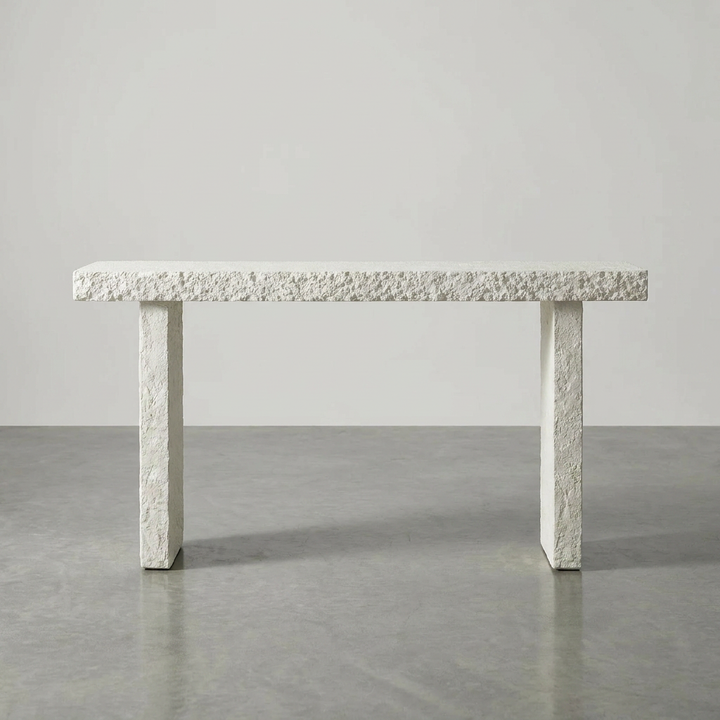 A modern rectangular stone table with a heavily textured, rough-surfaced light gray concrete or stone top and legs, set against a minimalist light gray studio background.