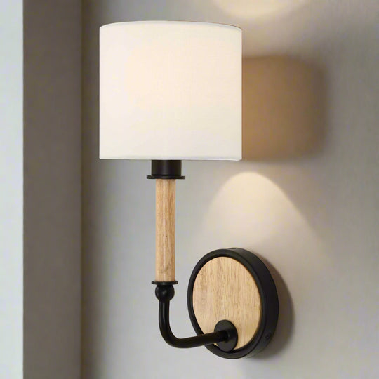 Wall-mounted lamp with white shade, wooden arm, and black metal base on a gray wall.