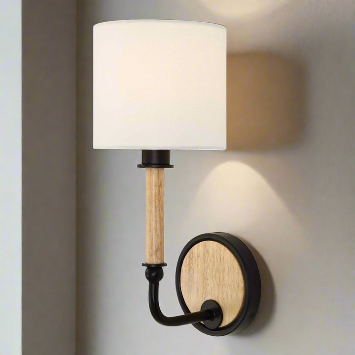 Wall-mounted lamp with white shade, wooden arm, and black metal base on a gray wall.